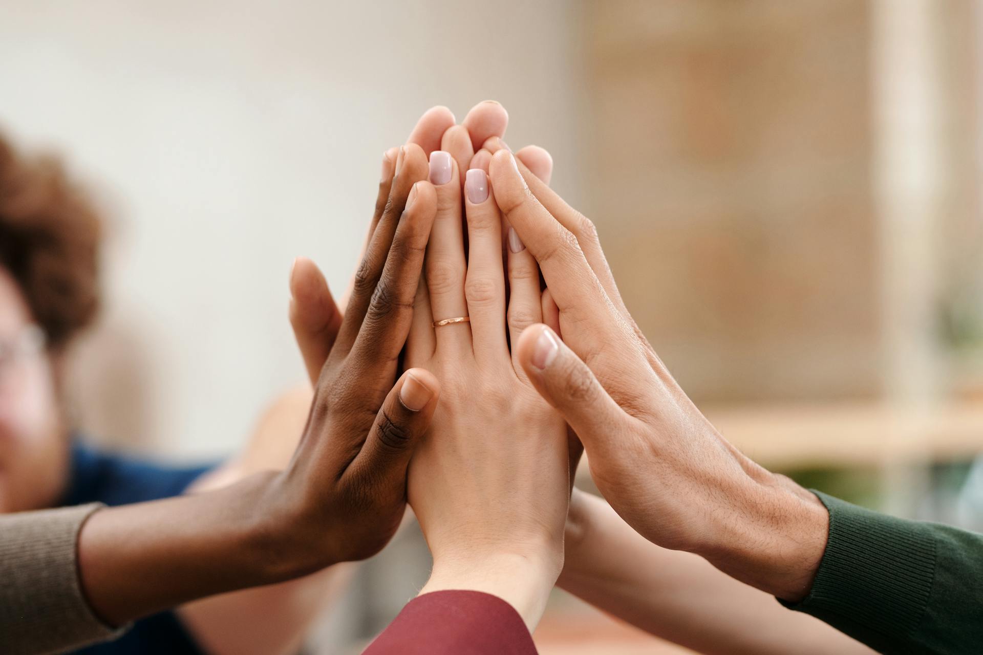 Several hands of different skin tones are stacked together in a close-up team gesture.